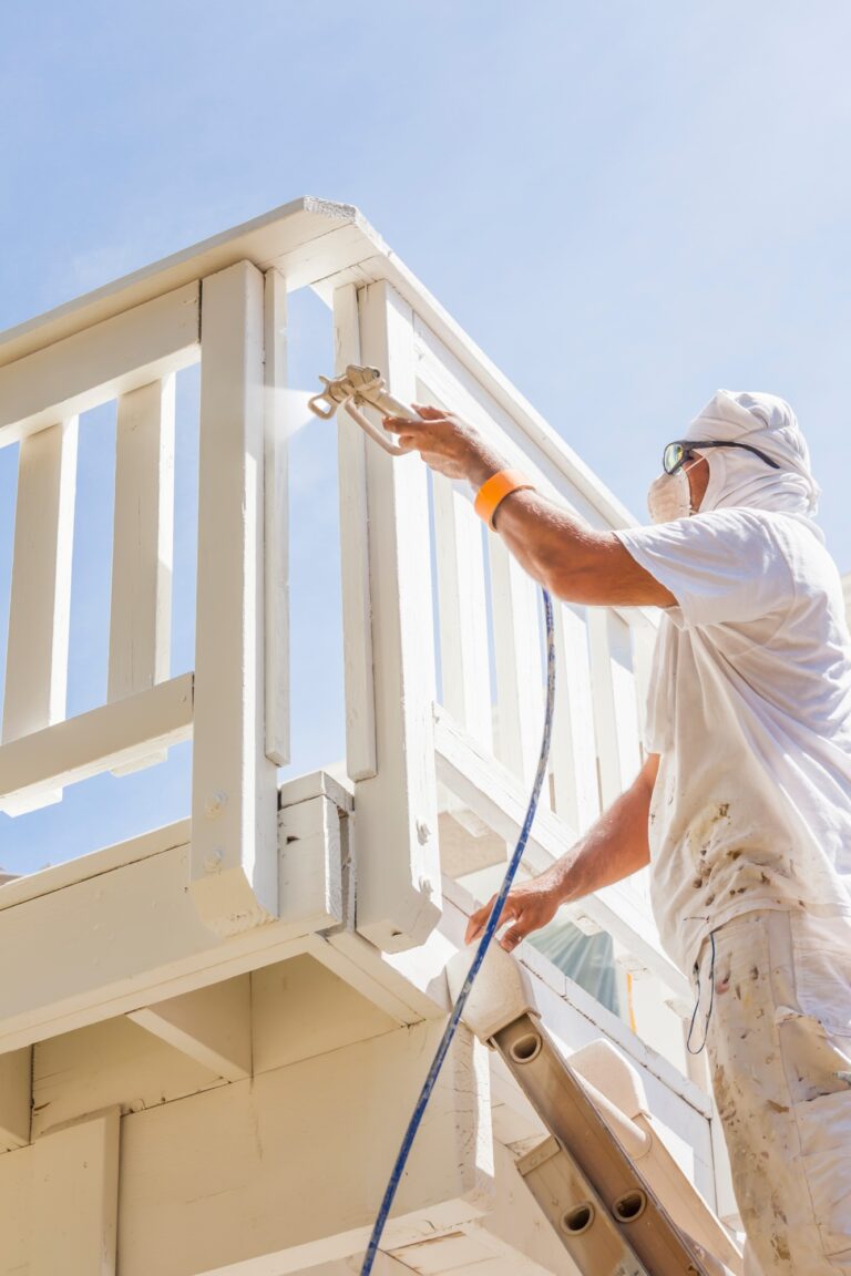Painter spraying white paint on wooden deck railing in Chico, CA